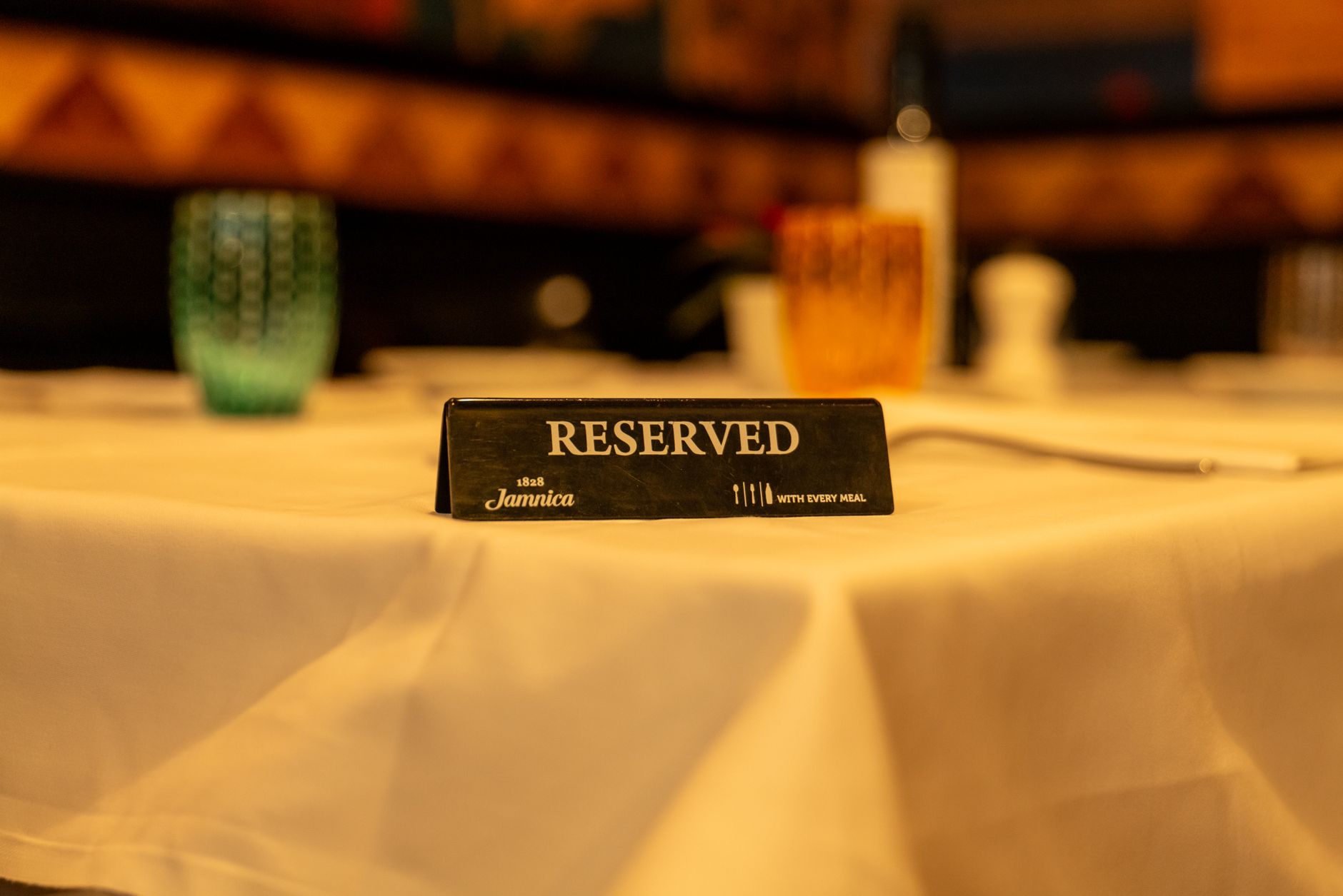 Tabliczka z napisem rezerwacja na białym obrusie w przyciemnionej restauracji